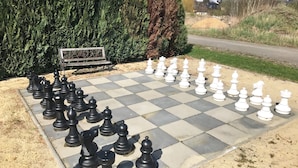 A large outdoor chessboard set up on a paved area with a bench and greenery in the background. - Holiday apartment PENZLIN in a maritime style near Radeberg (Leppersdorf)