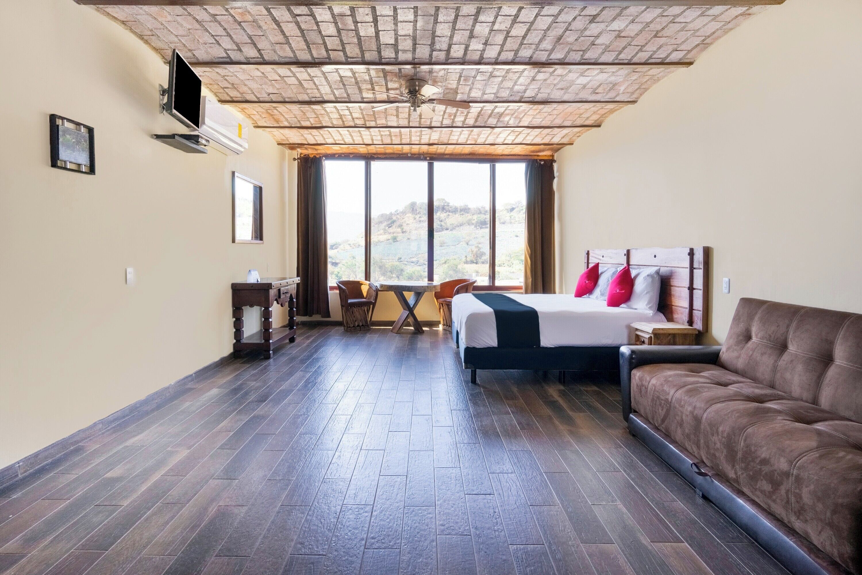 Habitación de hotel con cama, sofá, escritorio y silla. Amplia ventana con vistas al exterior.