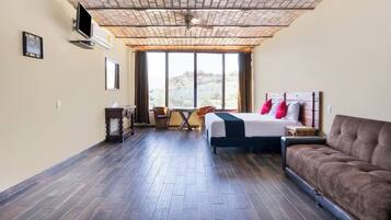 Habitación de hotel con cama, sofá, escritorio y silla. Amplia ventana con vistas al exterior.