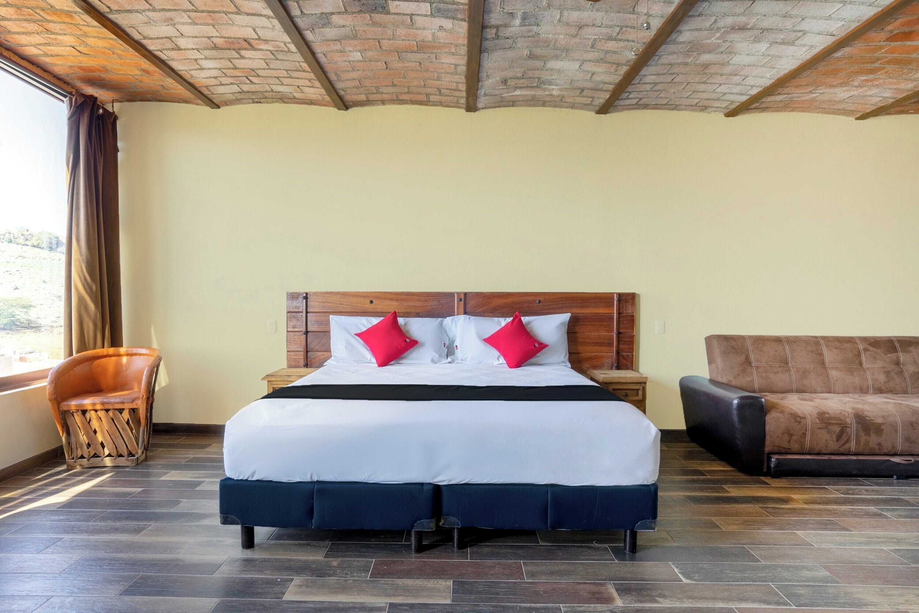 Una habitación de hotel con una cama grande, un cabecero de madera, un sofá de cuero marrón y una silla de madera.