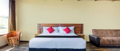 Una habitación de hotel con una cama grande, un cabecero de madera, un sofá de cuero marrón y una silla de madera.