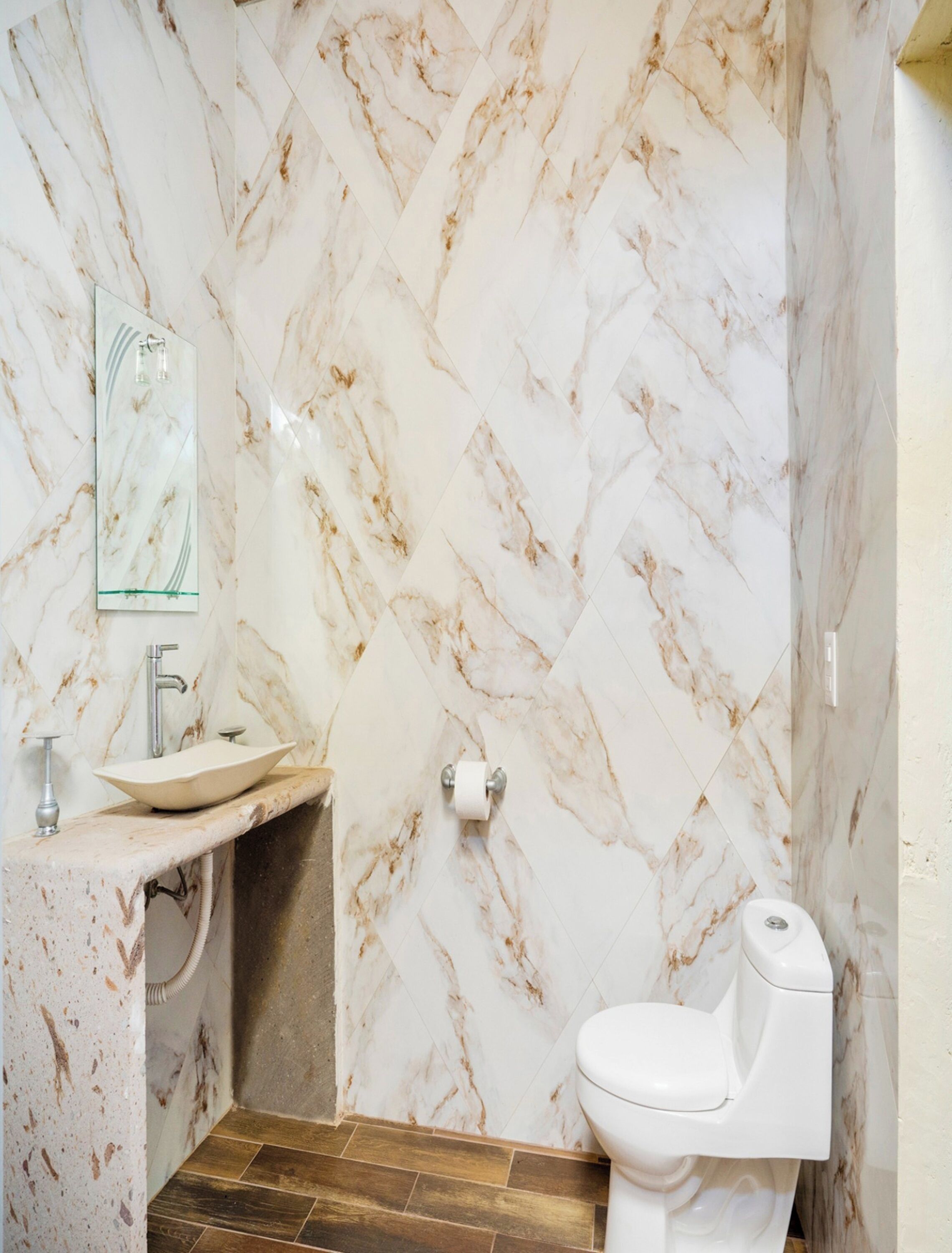 Un baño con pared de mármol, un lavamanos, un inodoro y un espejo.