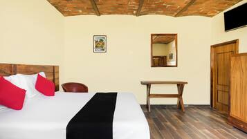 Habitación de hotel con cama, escritorio de madera, silla, espejo y armario.