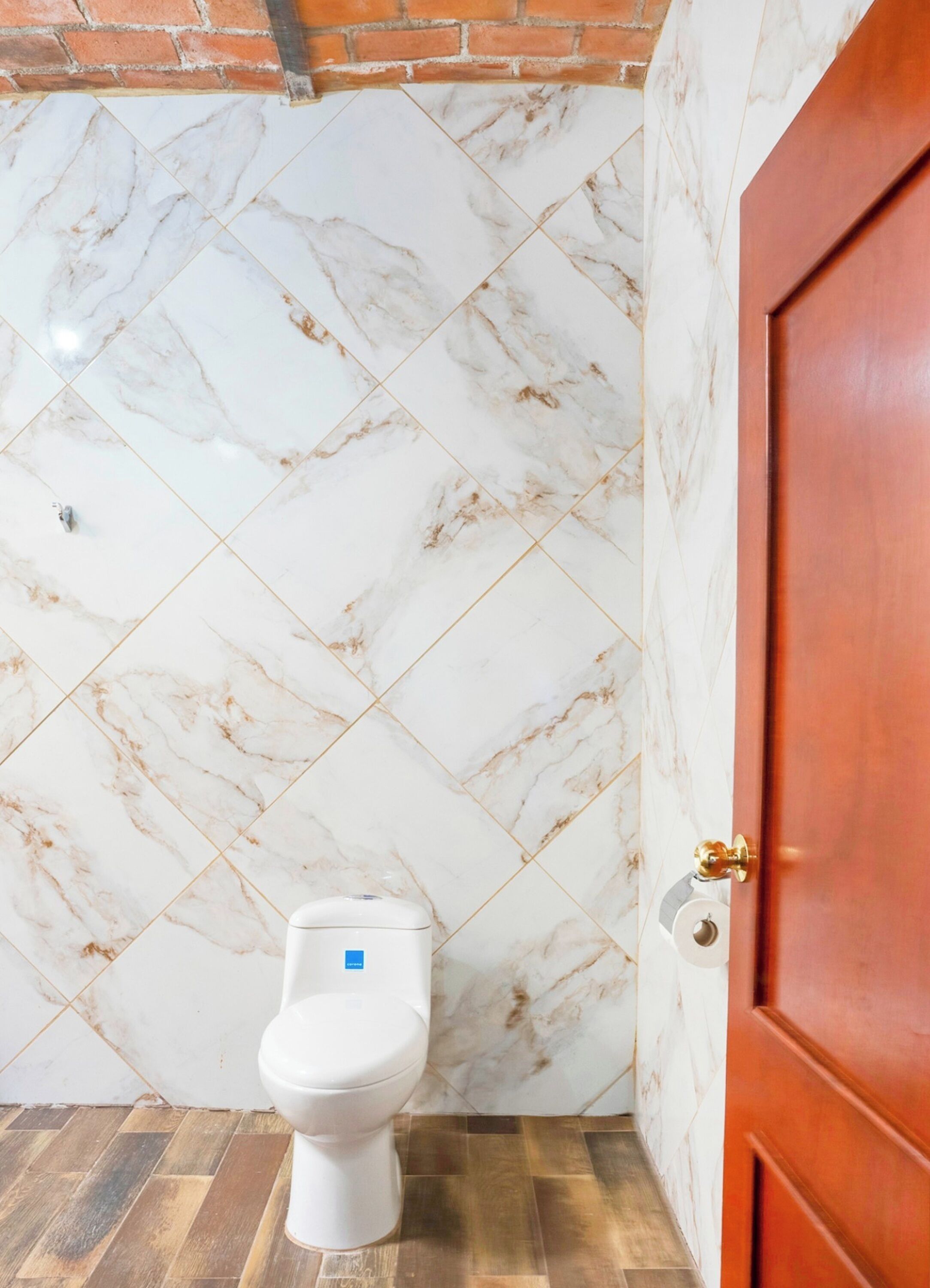 Une salle de bain avec des toilettes blanches, des murs à motifs de marbre et une porte en bois.