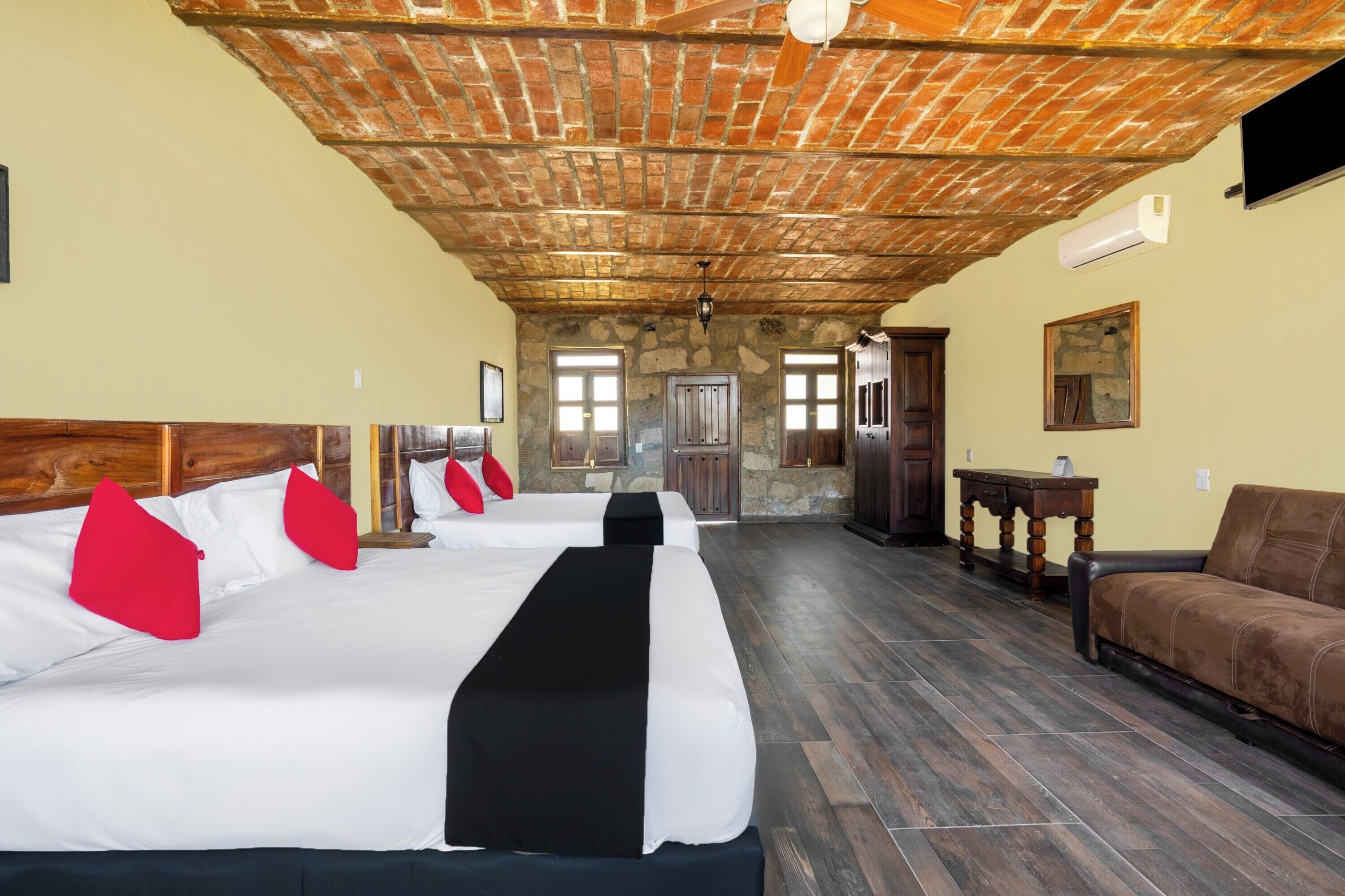 Quarto de hotel com três camas, teto de madeira, paredes de pedra e vista para o exterior.
