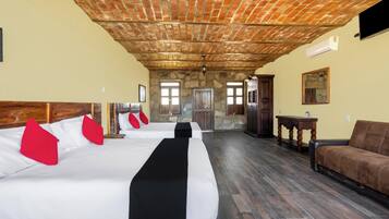 Quarto de hotel com três camas, teto de madeira, paredes de pedra e vista para o exterior.