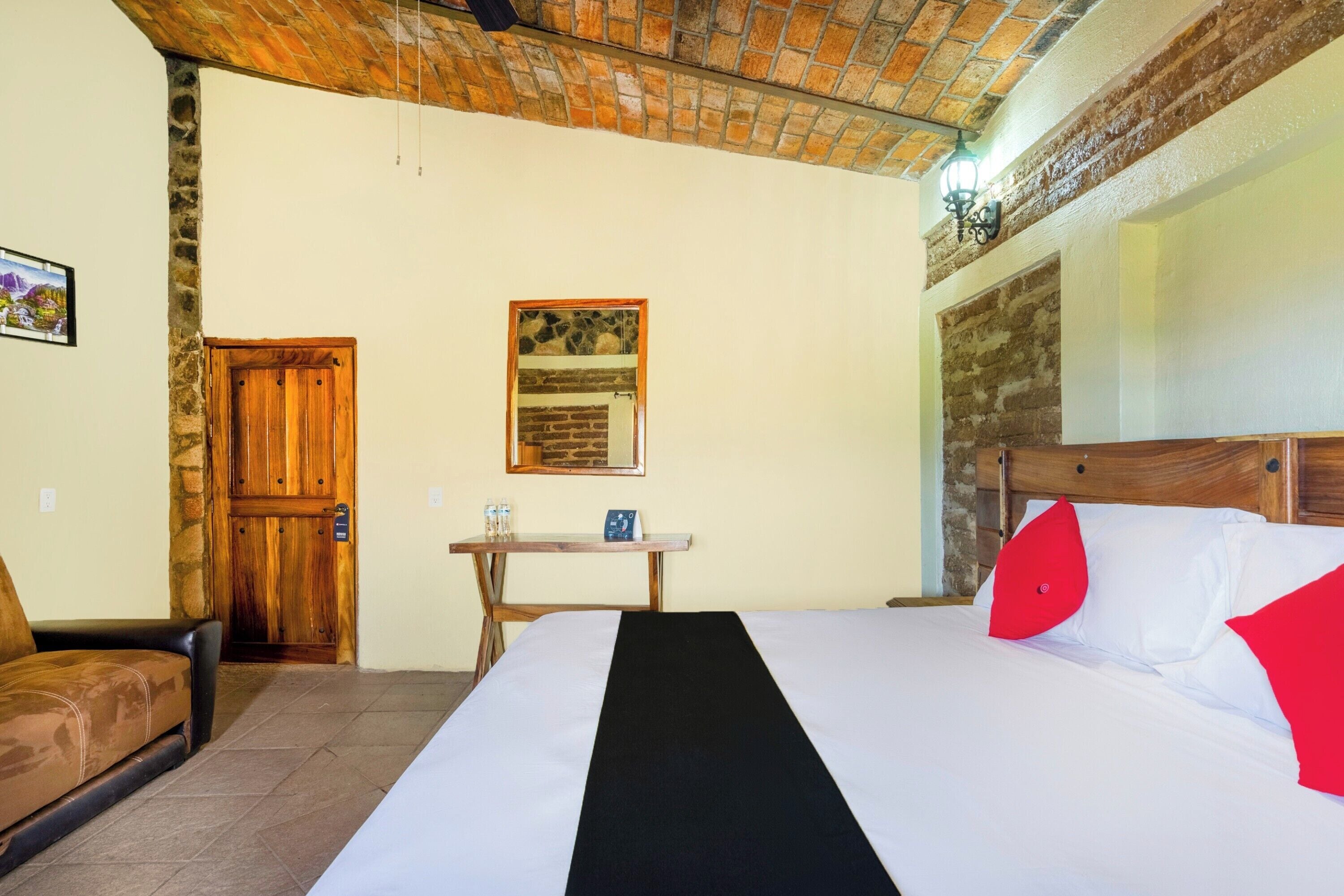 Una camera d'albergo con un letto, una porta di legno, un tavolino con una sedia e una parete in pietra.