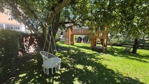 A wooden swing set, a small playhouse, and a bench in a sunny park area.