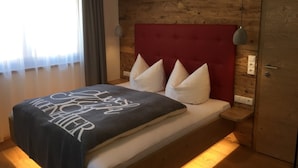 A hotel room with a wooden headboard, a bed with white pillows, and a dark blue blanket with white text. - Appartements Schweiberer, exclusive apartment Hochfügen (Ried im Zillertal)