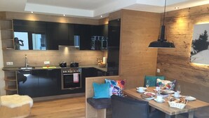 A modern kitchen with a central island, a dining area with a wooden table and chairs, and a cozy seating area with a white fur throw. - Appartements Schweiberer, exclusive apartment Hochfügen (Ried im Zillertal)