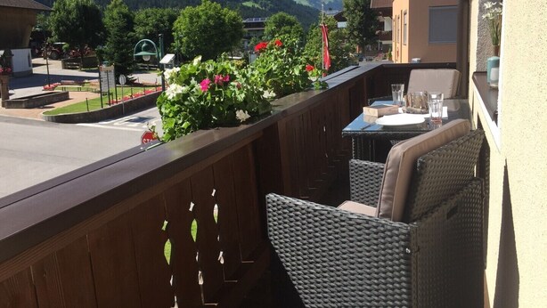 A balcony with wicker furniture, a view of a mountain, and a road with vehicles. - Appartements Schweiberer, exclusive apartment Hochfügen (Ried im Zillertal)