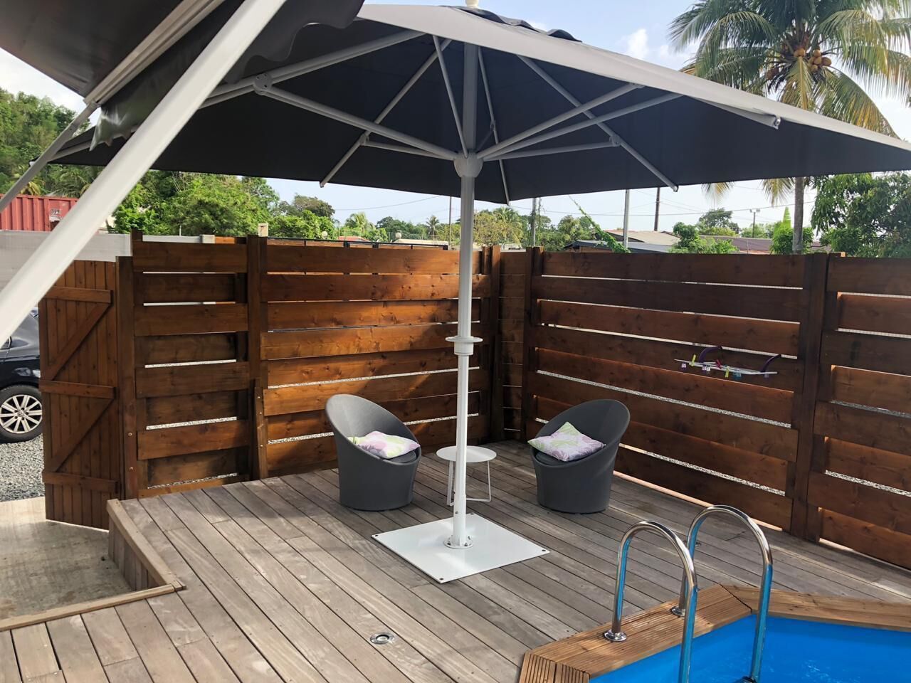 A wooden deck with a pool, two grey chairs, and a white umbrella.