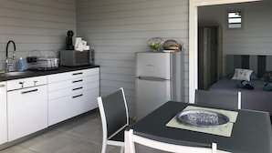 Cocina compacta con microondas, tostadora y refrigerador. Hay una mesa de comedor con una silla y una mesita con un plato decorativo.
