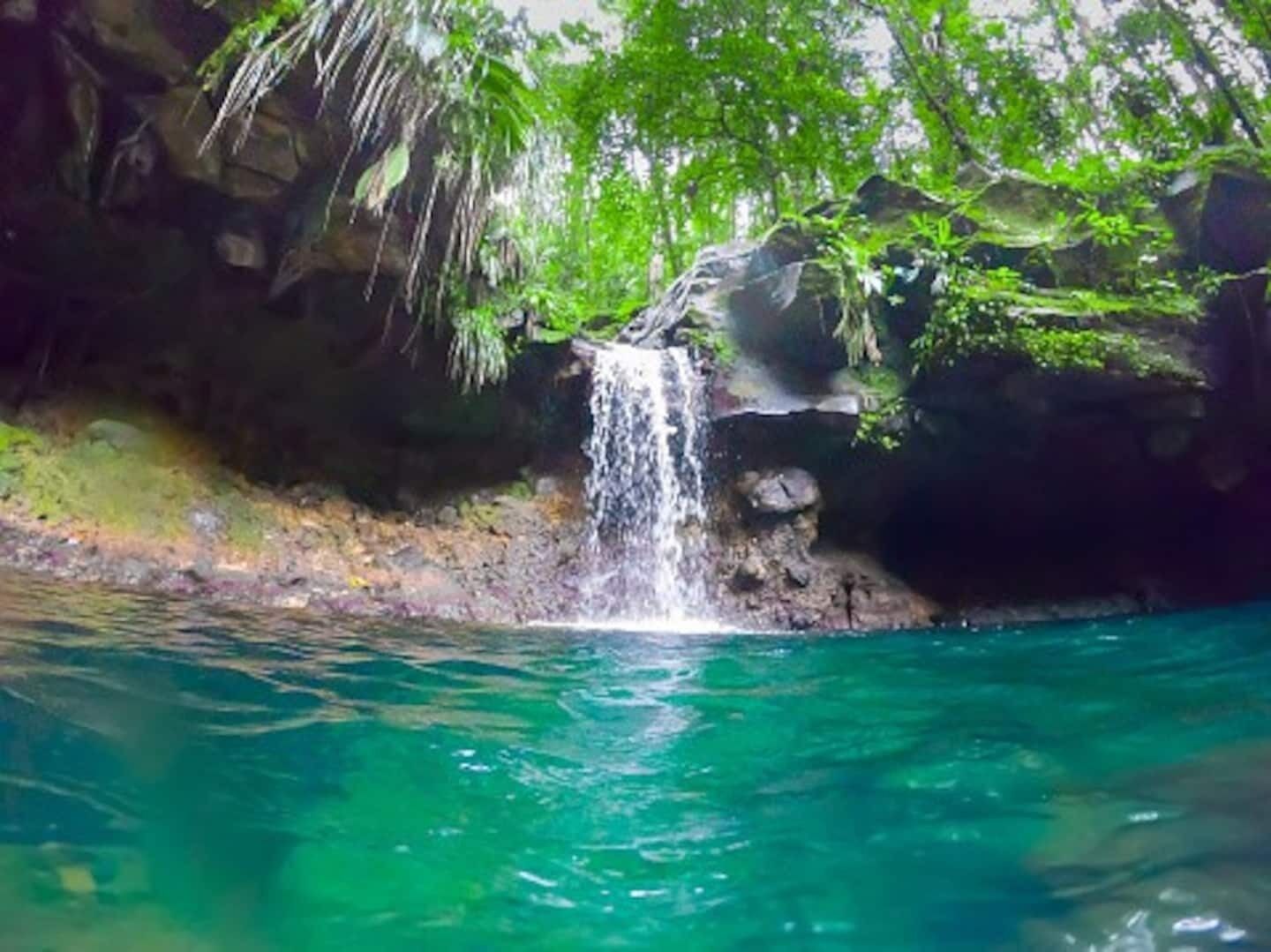 A waterfall cascading into clear blue water surrounded by rocky terrain and lush greenery.
