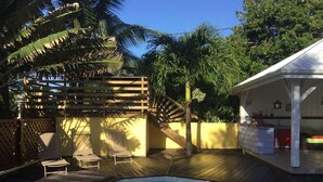 A pool area with a wooden deck, lounge chairs, and a covered seating area. - ti case gwada bungalow rentals "ti poisson" (Sainte-Anne)