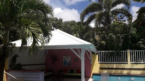 A small, colorful outdoor seating area with a pool, surrounded by palm trees and a white fence. - ti case gwada bungalow rentals "ti poisson" (Sainte-Anne)