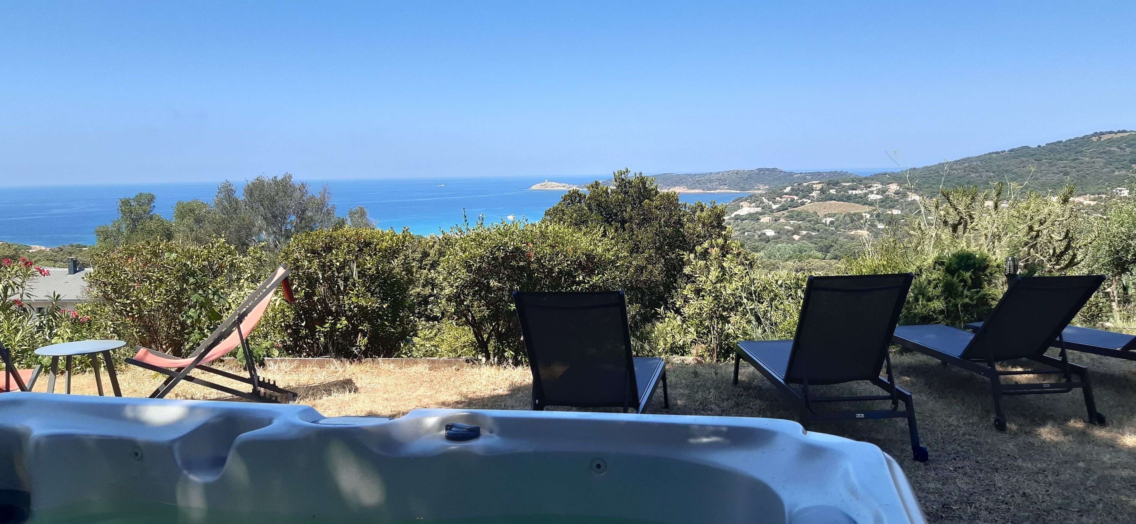 Un jacuzzi con dos sillas reclinables frente a una vista panorámica del mar y las colinas.
