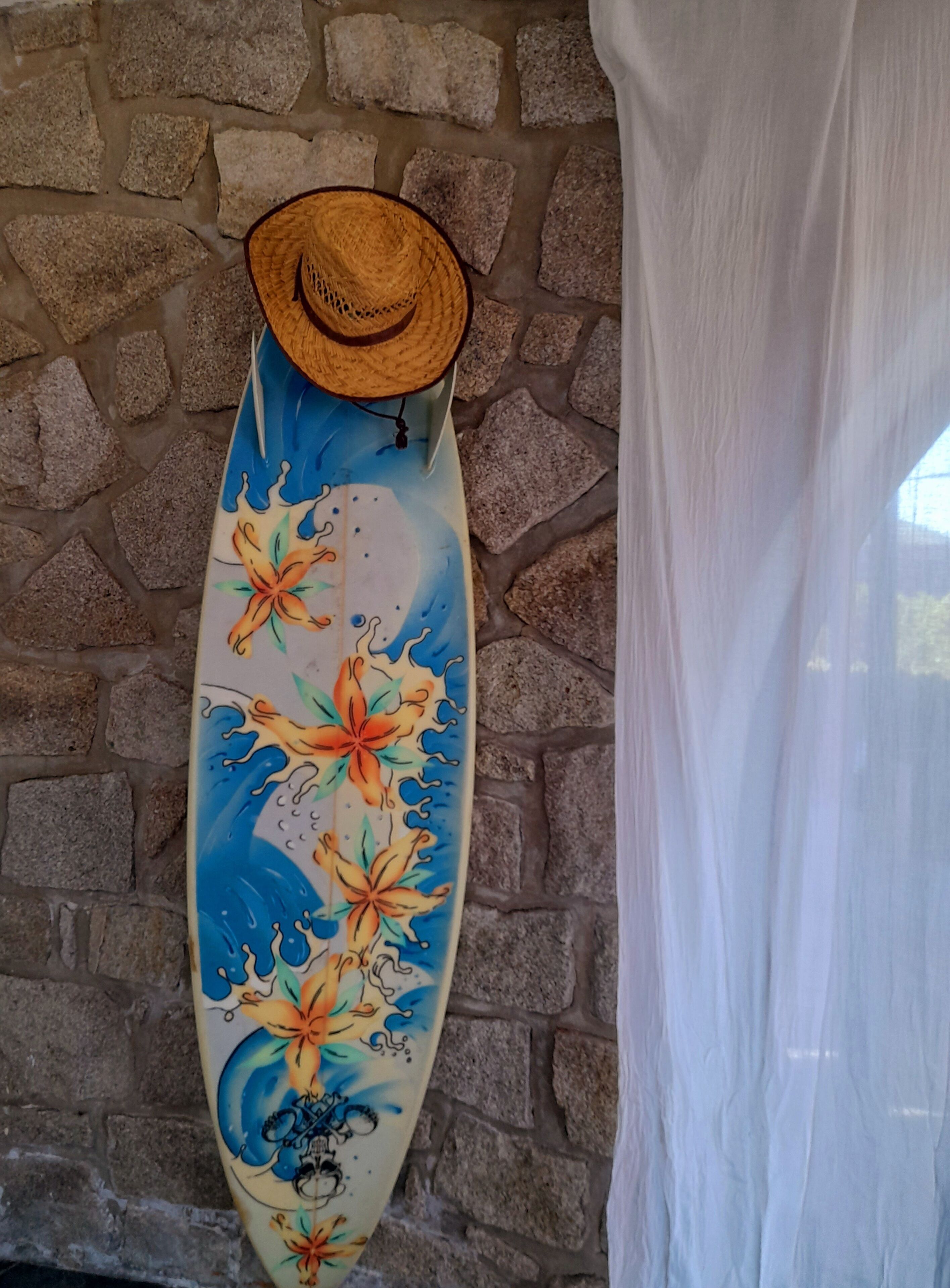 A surfboard with a floral design and a straw hat on top, mounted on a stone wall.