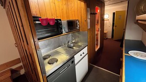 Una cocina compacta con paneles de madera, microondas integrado, pileta de acero inoxidable y lavavajillas.