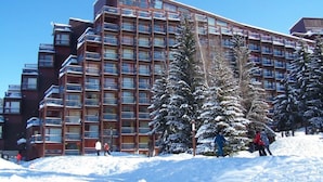 Un hotel de varios pisos con balcones, rodeado de árboles cubiertos de nieve.