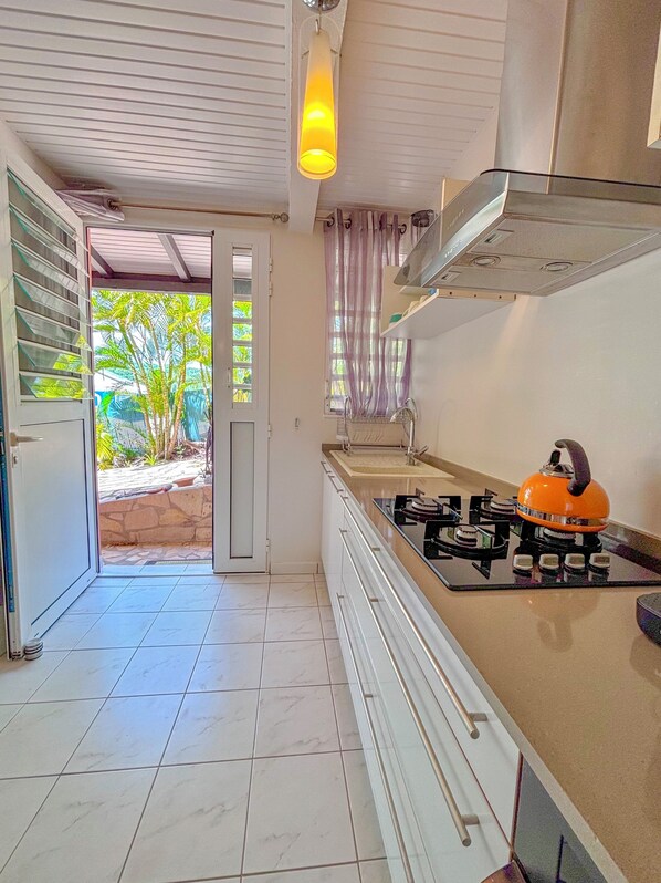 A kitchen with a gas stove, a sink, and a window with a view of greenery. - TI LARI La Villa WEST INDIES (Sainte Luce)