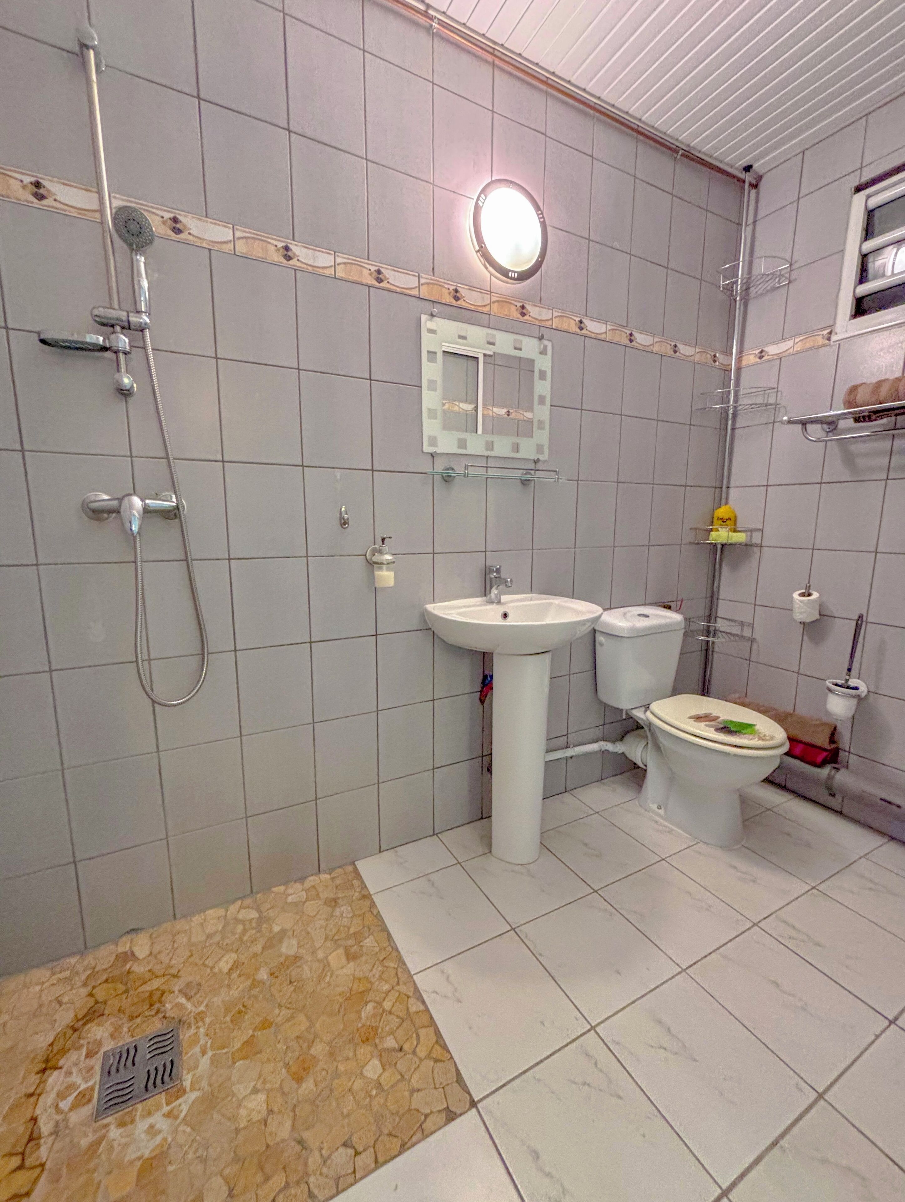 Een badkamer met een douche, wastafel, toilet en een spiegel.
