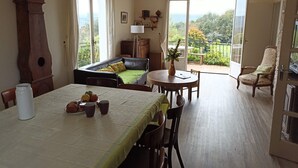 A dining area with a table set for four, a sofa, a balcony with a view, and a clock on the wall.