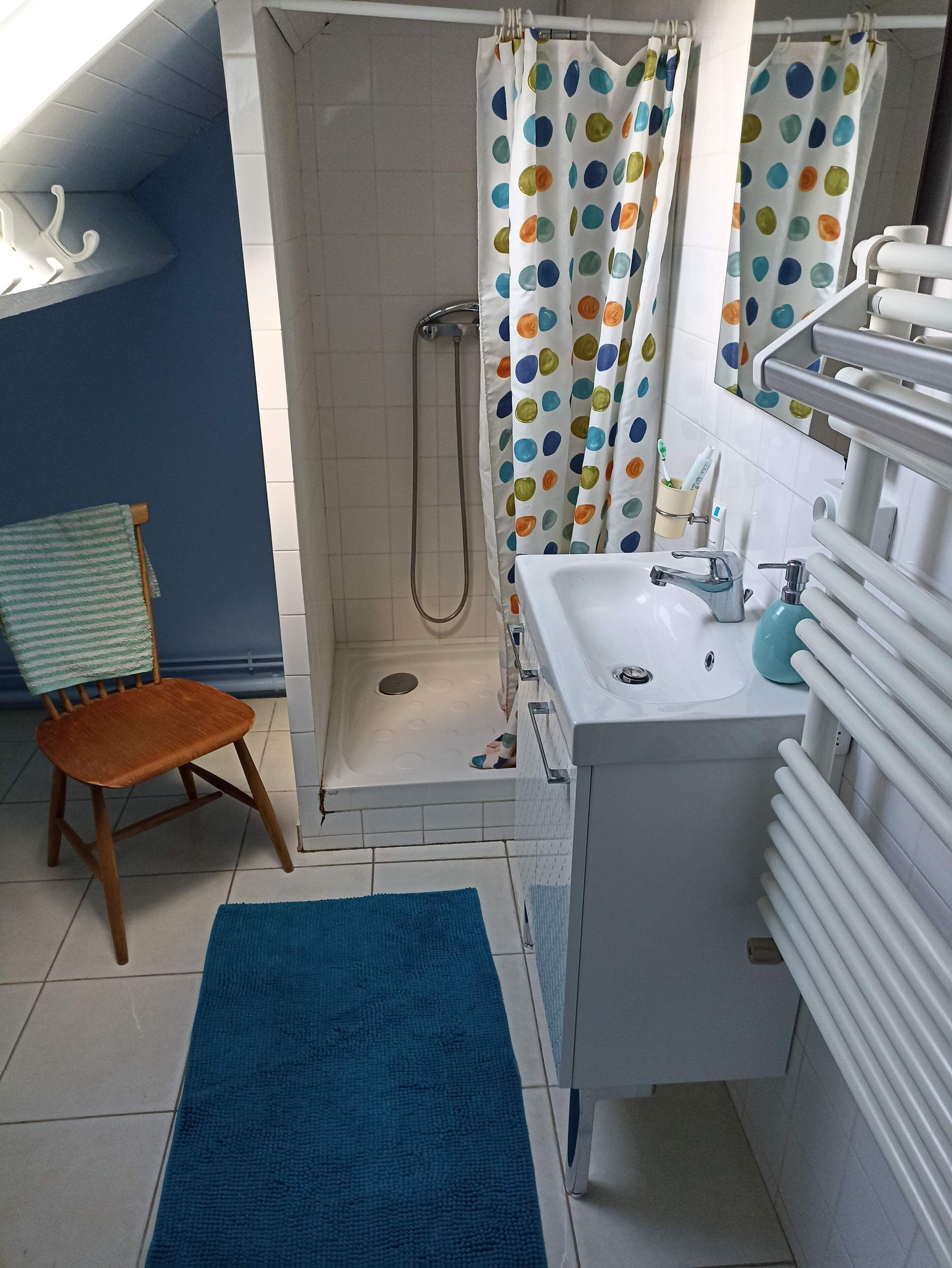 A bathroom with a shower, a sink, a chair, and a blue rug.