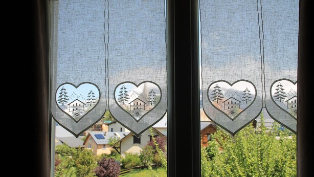A window with heart-shaped cutouts featuring mountain houses and trees. - 8/10 people cottage 110 m2  (les deux alpes)