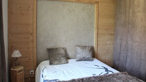A wooden room with a bed, two pillows, a nightstand with a lamp, and a curtain. - 8/10 people cottage 110 m2  (les deux alpes)