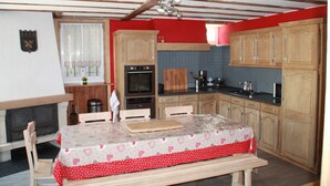 A compact kitchen with wooden cabinets, a dining table with a red tablecloth, and a built-in oven. - 8/10 people cottage 110 m2  (les deux alpes)