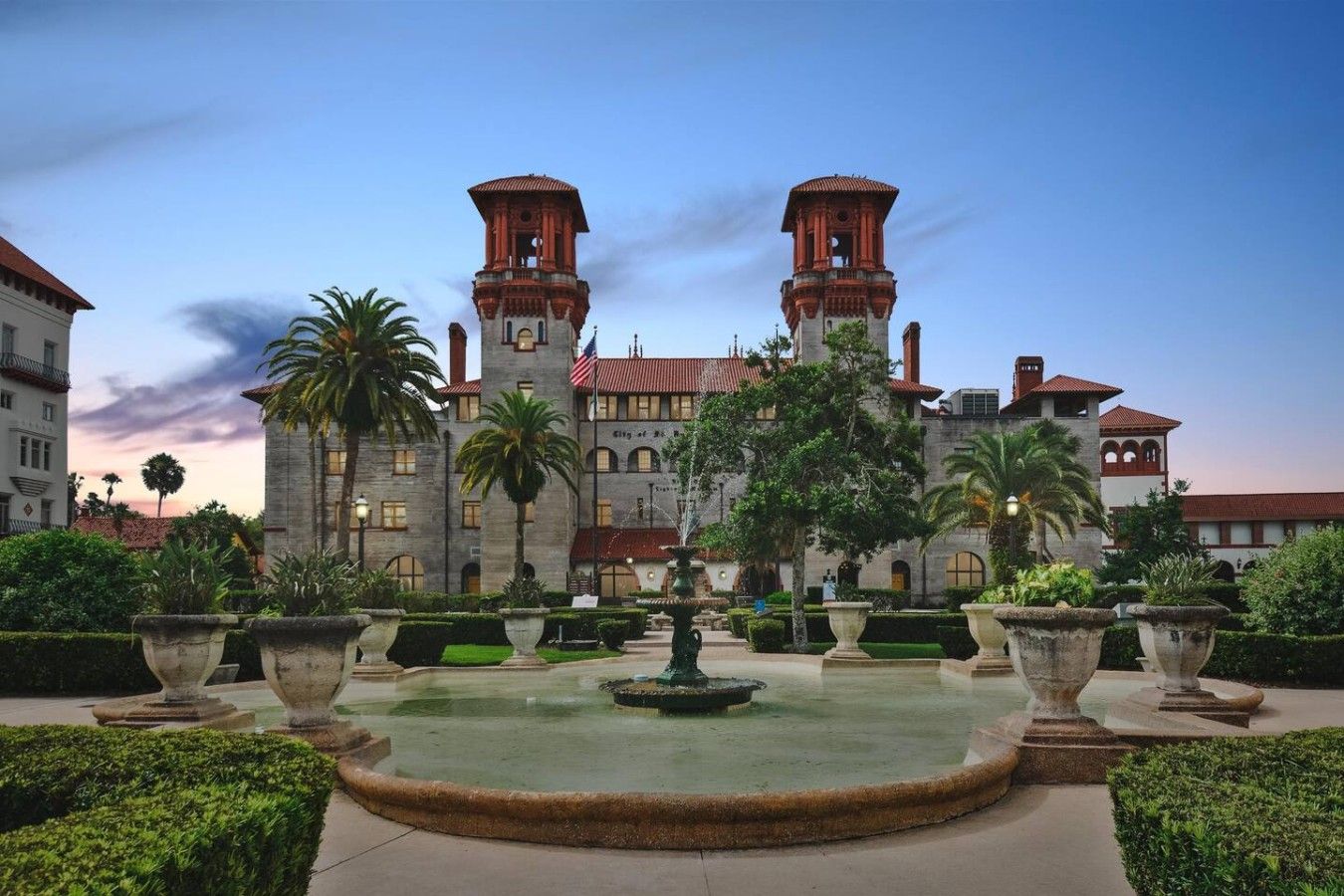 A large building with two towers, a fountain, and well-maintained gardens.