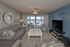 A living room with a sofa, armchairs, a coffee table, a TV, and a balcony with a view of the ocean. - SeeRay Shores 301 (St. Augustine Beach)