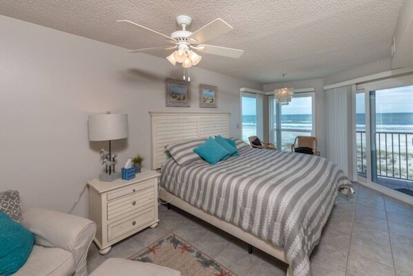 A bedroom with a bed, a nightstand, a lamp, a chair, and a view of the ocean.