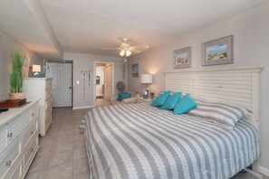 A bedroom with a bed, a ceiling fan, a dresser, and a door leading to another room. - SeeRay Shores 301 (St. Augustine Beach)