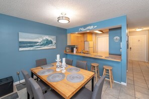 A dining area with a wooden table, grey chairs, and a blue wall with a wave painting.