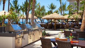 An outdoor dining area with thatched umbrellas, wicker furniture, and a grill station.