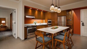 A modern kitchen with wooden cabinets, stainless steel appliances, and a dining area with a white table and patterned chairs.