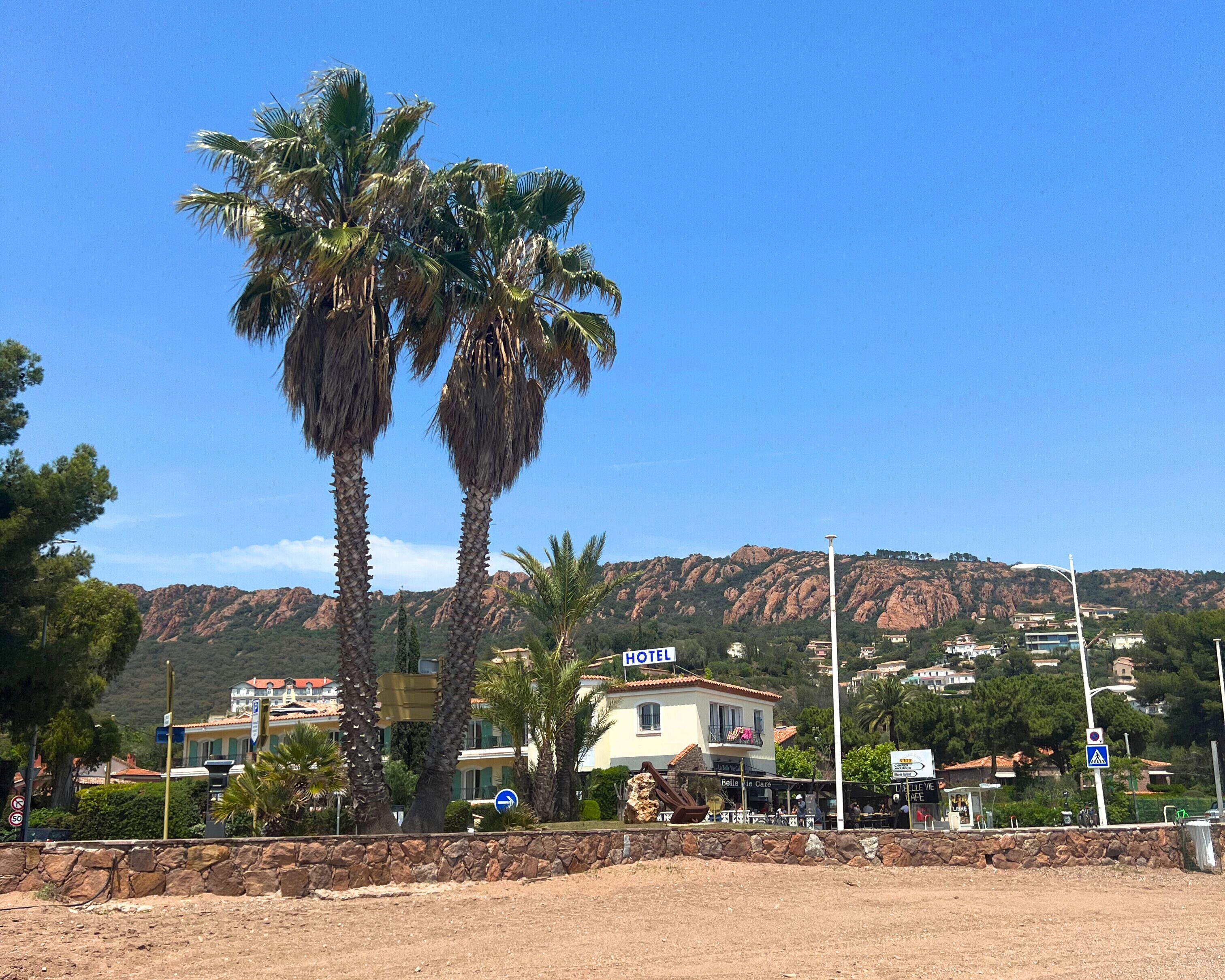 A hotel with a sign, palm trees, and a mountainous backdrop.
