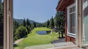 Näkymä ikkunasta, josta avautuu golfkenttä, jonka vieressä on lampi ja jota ympäröivät puut ja vuoret.