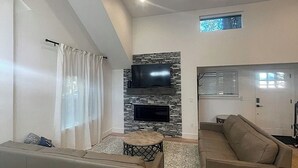 A living room with a flat-screen TV mounted on a stone wall, two sofas, a round coffee table, and a ceiling fan.