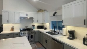 A modern kitchen with white cabinets, a gas stove, a microwave, and a coffee maker.