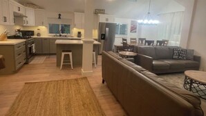 A modern kitchen with white cabinets, a central island, and a dining area with a sofa and table.
