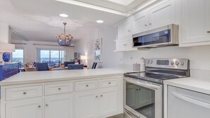 A modern kitchen with white cabinetry, a large island, stainless steel appliances, and a chandelier. - Direct Gulf Front Views ! Amazing Views ! (Sanibel)
