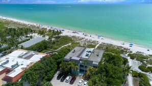An aerial view of a coastal hotel with a beach, parking area, and lush greenery. - Direct Gulf Front Views ! Amazing Views ! (Sanibel)