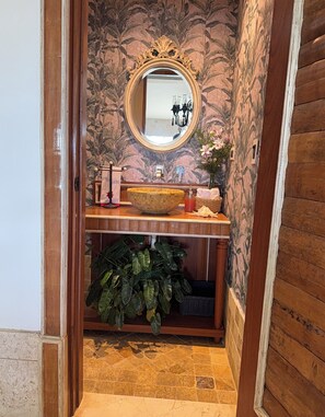 Een badkamer met een houten wastafelmeubel, een grote spiegel en bloemenbehang.
