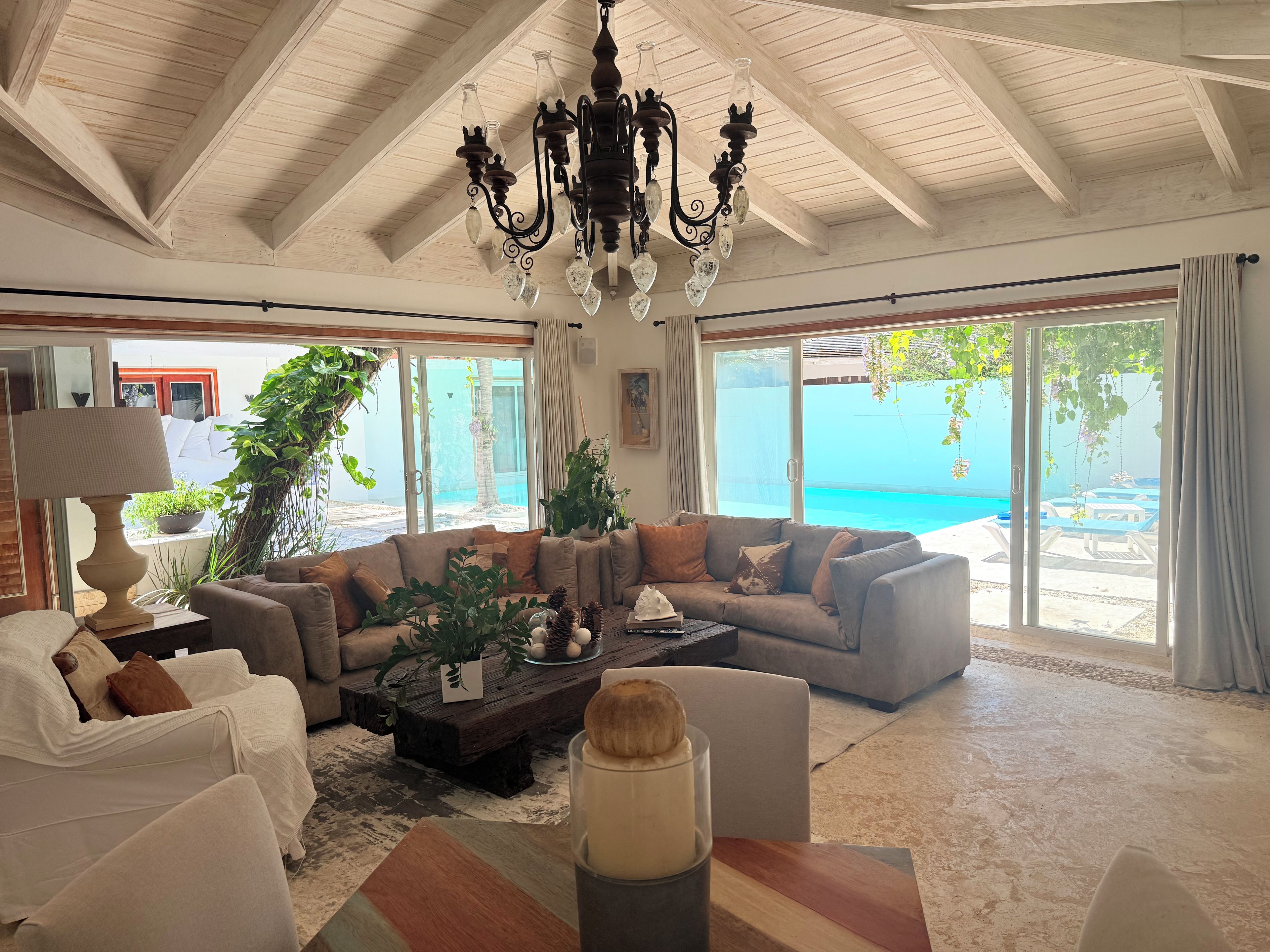 A spacious living room with a large window overlooking a pool, a chandelier, and a cozy seating area.