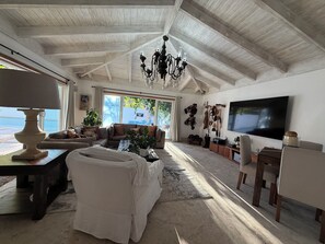A spacious living room with a high ceiling, a chandelier, a television, and a view of the outdoors.