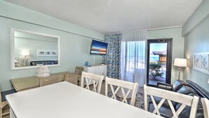 A room with a dining table, chairs, a television, a window with curtains, and a view of the outside. - Oceanfront - Poolside - Steps to Beach & Tiki Bar (Daytona Beach Shores)