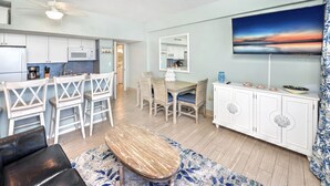 A modern living room with a dining area, a kitchen, and a large TV. - Oceanfront - Poolside - Steps to Beach & Tiki Bar (Daytona Beach Shores)